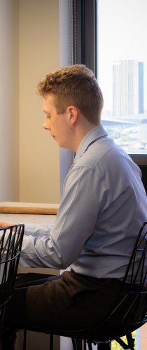 Professional in light blue shirt working at desk near window with city skyline view.