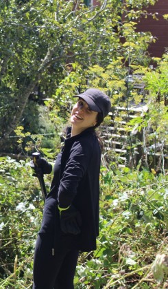 Person in dark clothing with cap looking upward in garden setting with greenery and steps.