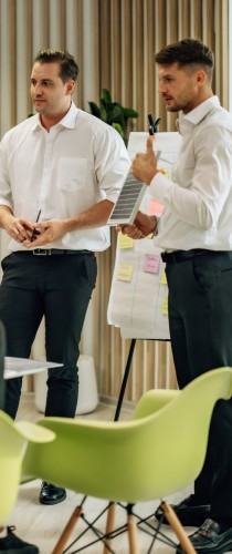 Two professionals in white shirts conversing in casual meeting area with contemporary green chairs.
