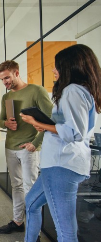 Colleagues walking through office space, man in green shirt and woman in blue shirt carrying tablet.