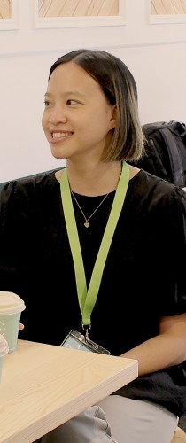 Woman with lanyard and black shirt smiling confidently at table with reusable coffee cup.