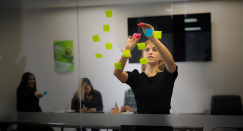 Faciltator placing colourful sticky notes on glass board during collaborative planning session with team members. 