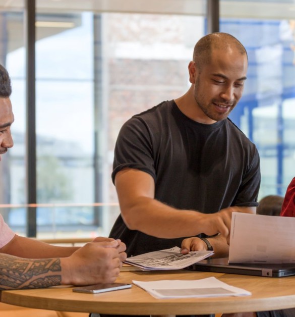 Three smiling team members reviewing documents together at a round table, sharing insights in bright modern office space with natural light.