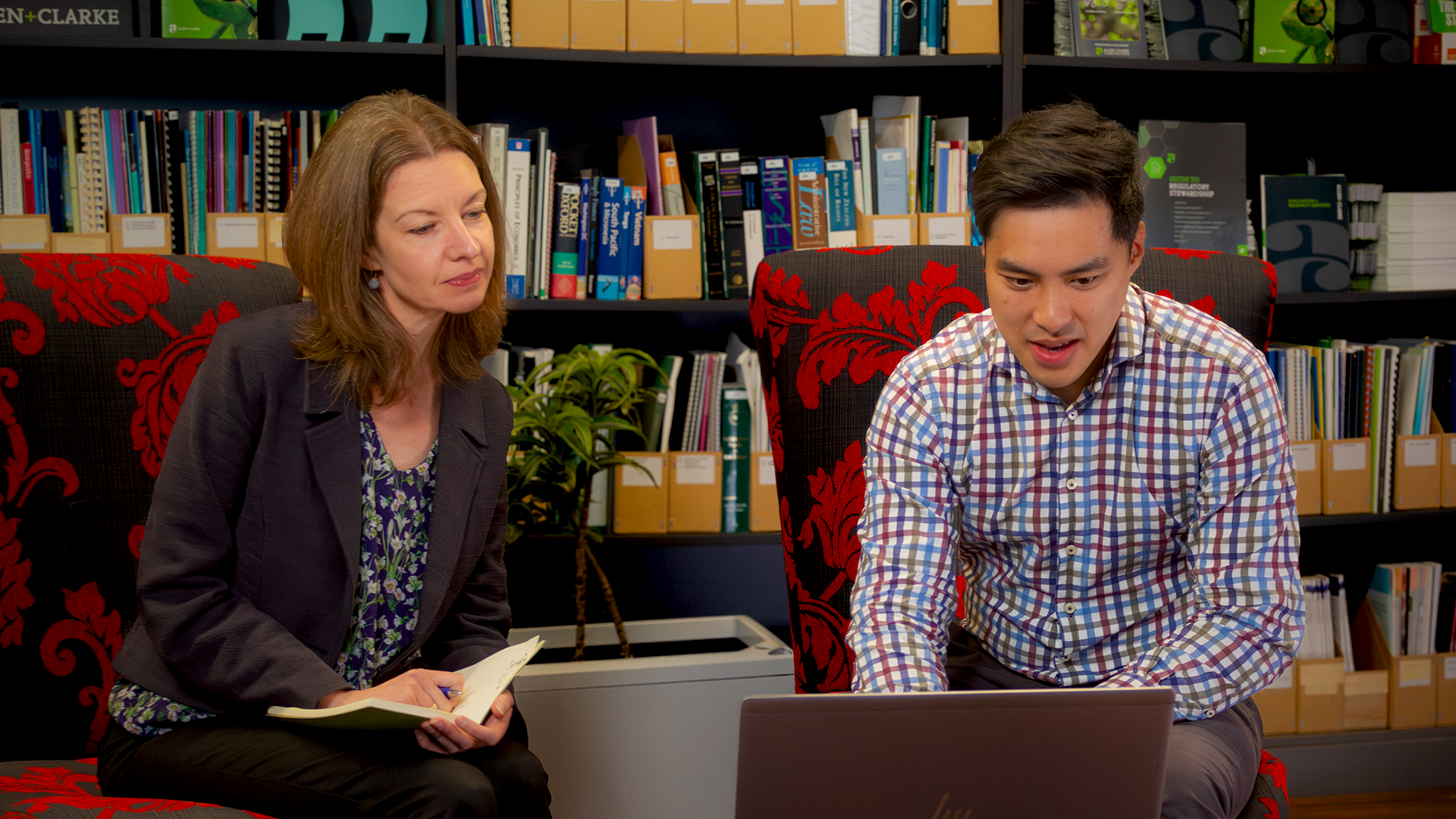 Woman and man working collaboratively on laptop in office area with bookshelves