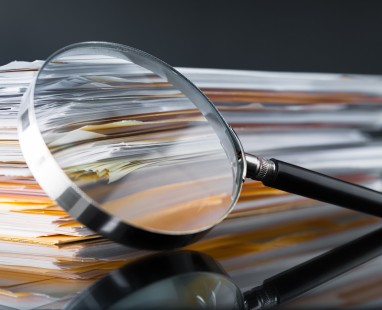 Magnifying glass resting on stack of documents, highlighting evidence-based approach to investigation and thorough analysis.
