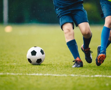 Young footballers in blue uniforms pursuing ball on green pitch, showcasing teamwork and active participation in youth sport.