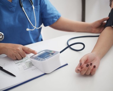 Healthcare professional in blue scrubs taking patient's blood pressure using digital monitor, demonstrating preventative health assessment.