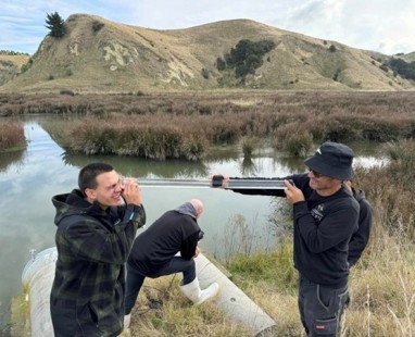 Researchers conducting field monitoring at wetland site, using specialized equipment to collect environmental data against backdrop of rolling hills.