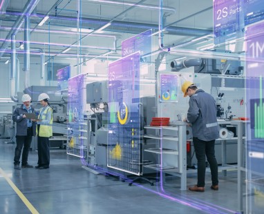 High-tech manufacturing facility with engineers monitoring equipment while augmented reality displays overlay production metrics and performance data.