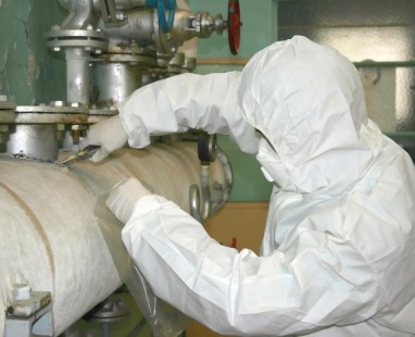 Technician in protective hazmat suit carefully inspecting industrial pipes and valves, demonstrating rigorous safety protocols in specialized facility