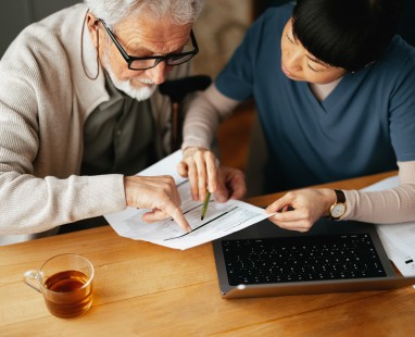 Older man and younger person collaborating over documents and laptop at desk