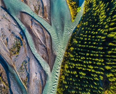 Aerial view of winding turquoise river channels flowing alongside dense green forest, capturing dramatic natural boundary between water systems and woodland in striking contrast
