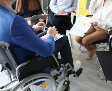 Person in wheelchair participating in business meeting with colleagues reviewing documents in office setting