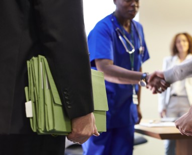 Healthcare provider in blue scrubs shaking hands with patient while colleague observes, depicting professional clinical consultation in medical setting