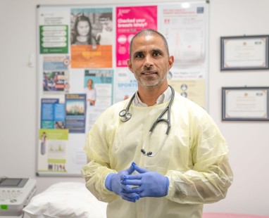 Healthcare professional in protective gown and gloves standing in medical office with health information posters
