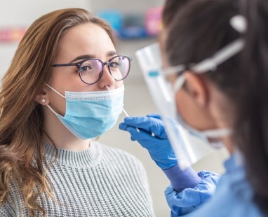 Healthcare worker administering nasal swab test to masked patient in medical clinic setting