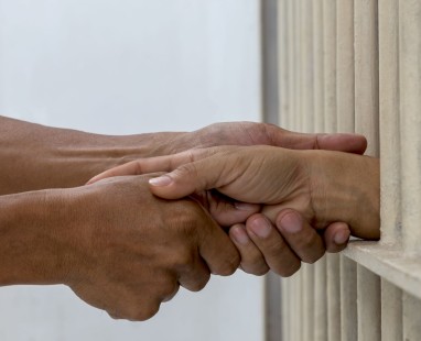 Two people shaking hands through prison cell bars.