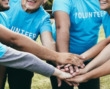 Group of volunteers in matching blue shirts placing hands together in team huddle showing community spirit