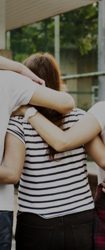 Group of young people with arms around each other's shoulders, viewed from behind, demonstrating unity and collaboration 