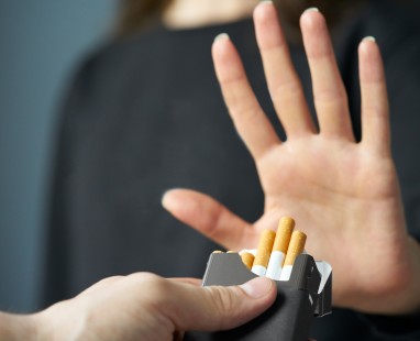 Hand raised refusing offered cigarettes against dark background