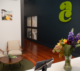 Welcoming office reception area featuring moss 'a+c' logo on navy wall, fresh flowers, and comfortable seating area with coastal artwork.