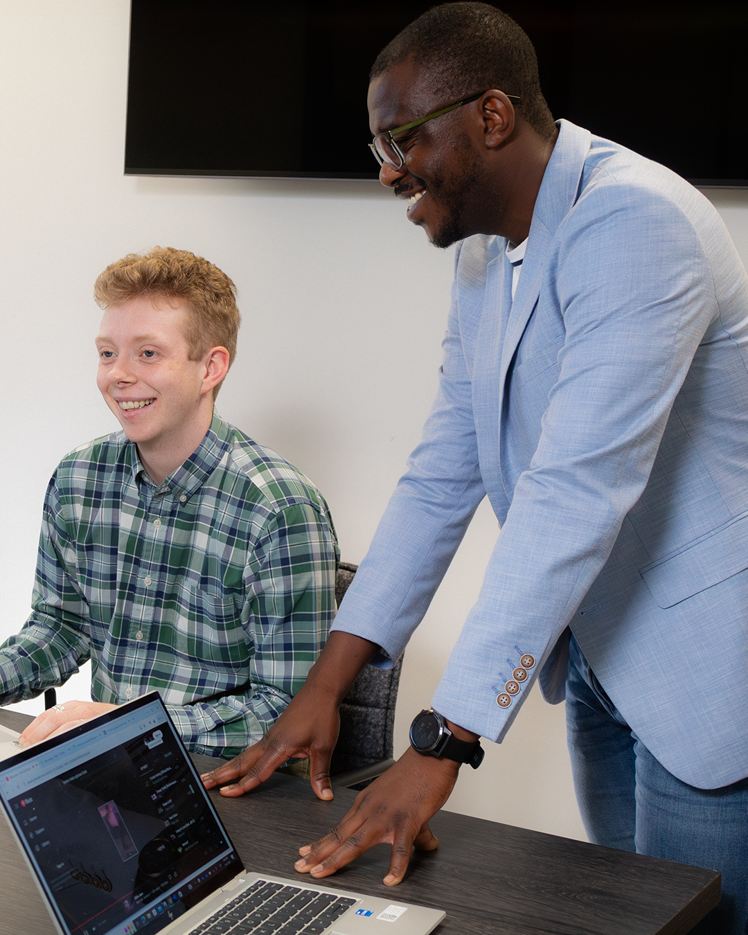 Collaborative consultation between professional in light blue blazer and young person, both engaged with laptop content in meeting space.