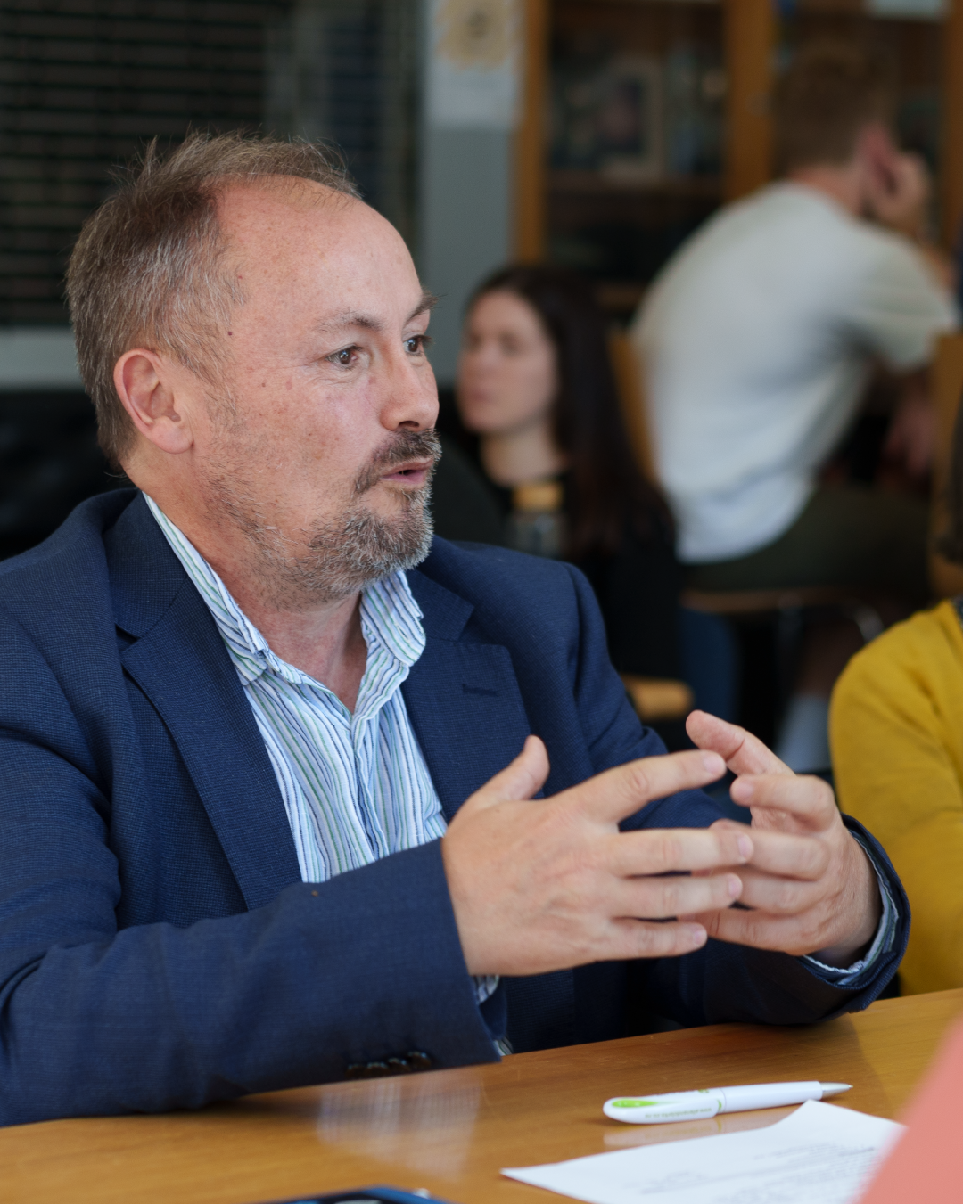 Team member in blue suit jacket actively contributing during meeting, gesturing to emphasize key points at conference table.