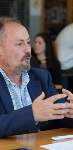 Team member in blue suit jacket actively contributing during meeting, gesturing to emphasize key points at conference table.