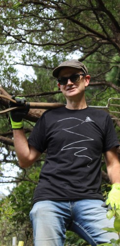 Volunteer worker in protective gear carrying spade in forested area. 