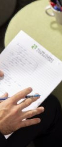 Hands reviewing document with Allen + Clarke letterhead, taking notes during consultation session. 