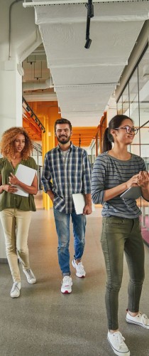 Three team members walking purposefully through corridor with refreshments. 
