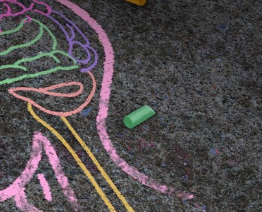 Colorful sidewalk chalk drawing of a human profile with brain regions outlined in pink, yellow, and green, symbolizing mental health awareness.
