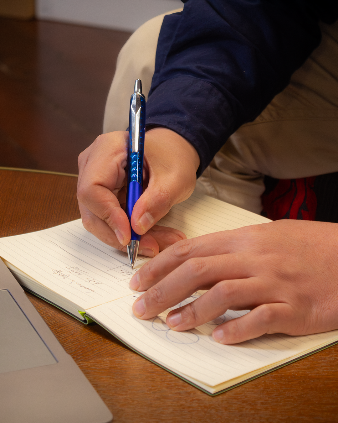 Close-up of hand writing in notebook with blue pen, capturing ideas and notes