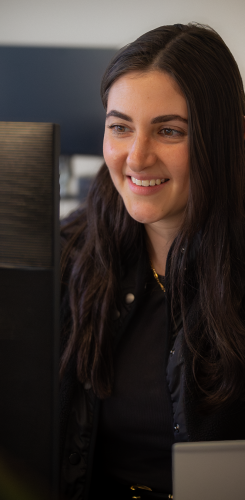Woman with dark hair smiling at computer monitor in office setting