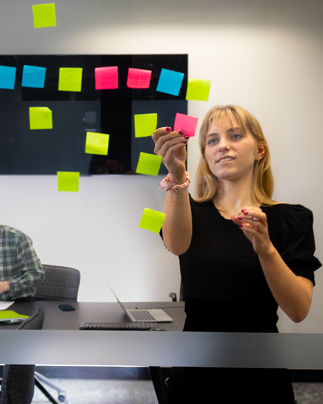 Woman placing colorful sticky notes on glass surface during brainstorming session