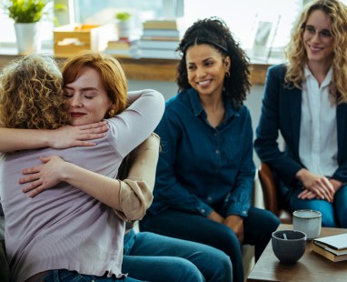 Women embracing supportively in group therapy or counselling session