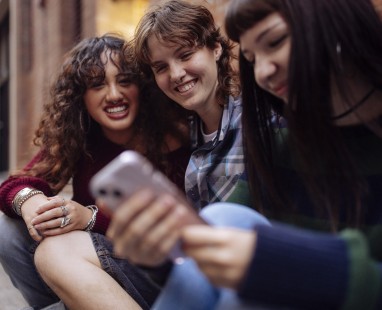 Three diverse friends huddled together looking at a smartphone and smiling. 