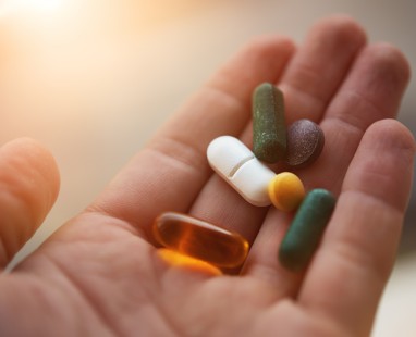 An open hand holding an assortment of dietary supplements and pills, including capsules, tablets, and a gel softgel.